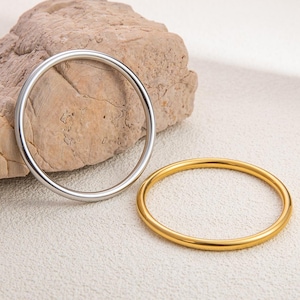 May include: Two plain bangles, one silver and one gold, are shown on a neutral background. The bangles are circular and have a smooth, polished finish. The gold bangle has a warm, shiny appearance, while the silver bangle has a cool, metallic sheen.