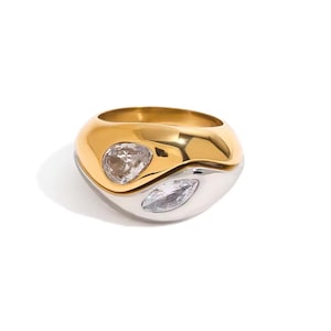 May include: A two-tone ring with a gold top and a silver bottom. The ring features two clear, teardrop-shaped gemstones. The ring is a bold, modern piece of jewelry.
