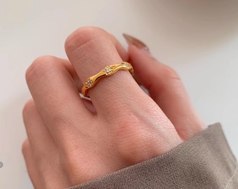 Peut inclure: Une bague dorée au design ondulé, sertie de petites pierres précieuses claires. La bague est portée au doigt, mettant en valeur ses détails complexes et ses accents scintillants. Le design de la bague est élégant et accrocheur.