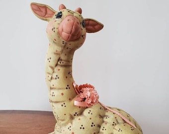 May include: A ceramic giraffe figurine with a light green and brown spotted pattern. The giraffe has a pink nose and a pink flower on its neck.