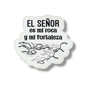 May include: A white sticker with the text "EL SEÑOR es mi roca y mi fortaleza" in black, above a black and white illustration of a landscape with water and rocks. The sticker has a white border and a shadow.