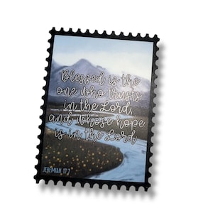 May include: A rectangular sticker with a black border. The image shows a landscape with mountains and a river. The text reads "Blessed is the one who trusts in the Lord, and whose hope is in the Lord". The scripture reference Jeremiah 17:7 is also included.