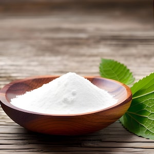 May include: A white powder in a wooden bowl, with green leaves in the background.