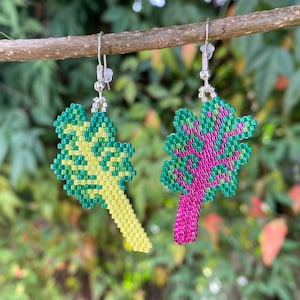May include: A pair of beaded earrings, one green and yellow, the other pink and green. The earrings are hanging from a branch.