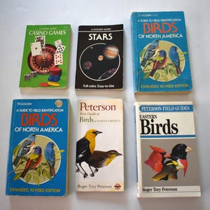 May include: A collection of six vintage field guide books arranged in two rows. The books feature titles including Casino Games, Stars, Birds of North America, and Eastern Birds, with colorful illustrations of birds, space, and gambling imagery on covers.