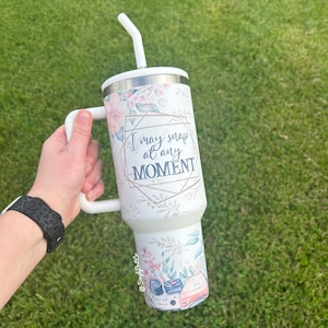 May include: White stainless steel tumbler with a floral design and the text "I may snap at any MOMENT". The tumbler has a white lid and a white straw.