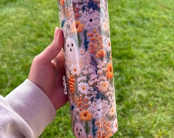 May include: A white and orange floral print tumbler with a ghost design. The tumbler has a clear lid and a straw.
