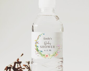 May include: A clear plastic water bottle with a white label. The label reads "Emily's Baby Shower" with a floral wreath and the date "6.5.XX". The bottle is on a woven mat. The bottle contains water.