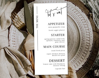 May include: A white menu card with black text on a wooden table setting. The menu card has the title "Let's Eat" and lists appetizers, starters, main courses, and desserts. The menu items include mini gazpacho soup, spring greens salad, wood fired pizza, and lemon cake with blueberry mousse filling.