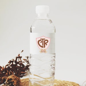 May include: A clear plastic water bottle with a white label featuring a pink shield with the letters "CTR" in brown. The shield is surrounded by a floral design.