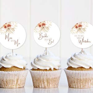 May include: Three cupcakes with white frosting topped with round paper circles. The circles feature a floral design with the text "Miss to Mrs.", "Bride to Be!" and "Future Mrs. Whitaker".