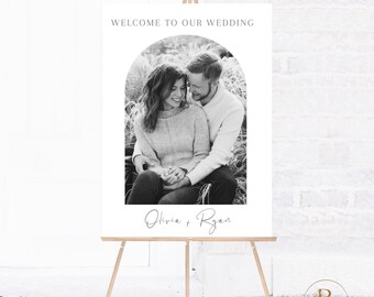 May include: Black and white wedding welcome sign with an archway design featuring a photo of a couple. The text reads "Welcome to our wedding" and "Olivia + Ryan".