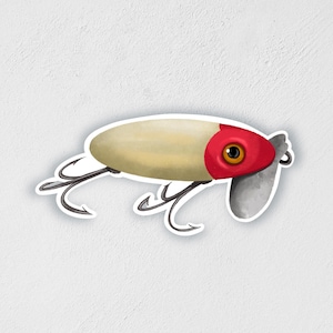 May include: A white and red fishing lure with two treble hooks. The lure has a red head with a black eye and a white body.