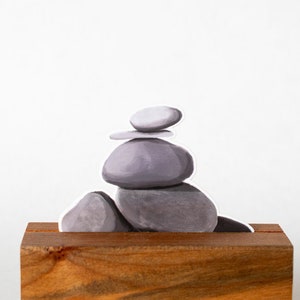 May include: A stack of gray stones balanced on a wooden base. The stones are arranged in a pyramid shape, with the smallest stone on top.