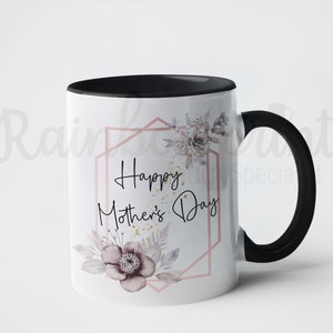 Op de afbeelding: Witte keramische mok met een zwarte rand en handvat. De mok heeft een bloemenmotief met een roze geometrisch frame en de tekst "Happy Mother's Day".