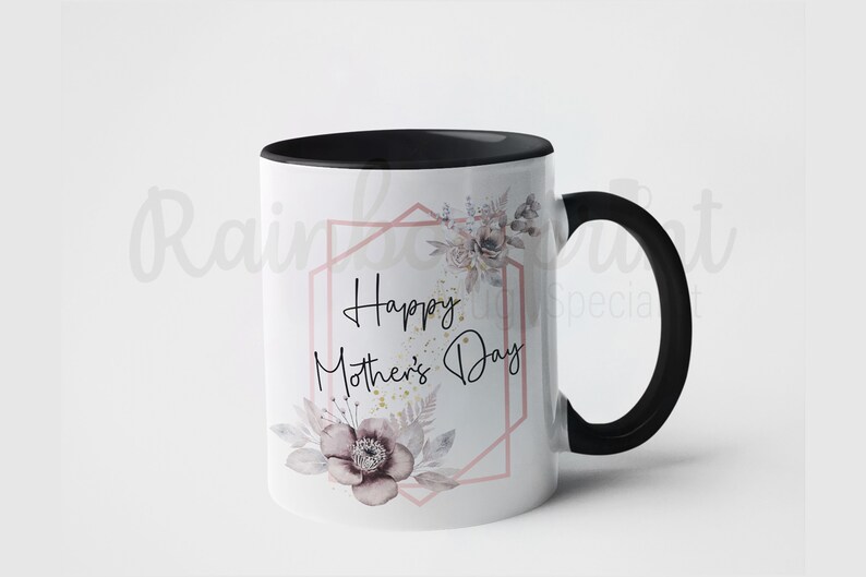 Op de afbeelding: Witte keramische mok met een zwarte rand en handvat. De mok heeft een bloemenmotief met een roze geometrisch frame en de tekst "Happy Mother's Day".