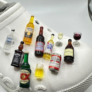 May include: A collection of miniature liquor bottles and cans, including Corona Extra, Absolut Vodka, Jack Daniels, Dos Equis, Budweiser, Pabst Blue Ribbon, Hennessy VSOP, and a glass of red wine. The miniature bottles and cans are arranged on a white surface.