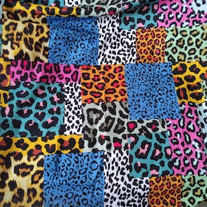 Puede incluir: Un textil de patchwork con un diseño de estampado de leopardo. La tela está compuesta por varios cuadrados, cada uno mostrando una paleta de colores y una variación de patrón diferente. Los colores incluyen amarillo, rosa, azul y naranja.