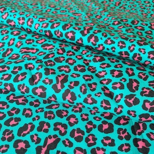 Peut inclure: Tissu turquoise avec un motif léopard répété en noir et rose. Le tissu est plié, révélant sa texture et son motif. Ce textile pourrait être utilisé pour des vêtements, des accessoires ou des projets de décoration intérieure.