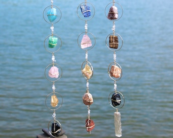 Peut inclure: Trois mobiles suspendus en cristal avec des anneaux dorés et des cristaux de différentes couleurs. Les mobiles sont suspendus à une branche au-dessus d'une étendue d'eau.