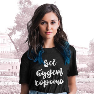 May include: A dark heather grey t-shirt with the text "всё будет хорошо" in white lettering.