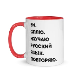 Puede incluir: Taza de cerámica blanca con borde rojo. La taza tiene texto negro que dice "EM. СПЛИКО. ИЗУЧАЮ РУССКИЙ ЯЗЫК. ПОВТОРЯЮ."