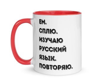 Puede incluir: Taza de cerámica blanca con borde rojo. La taza tiene texto negro que dice "EM. СПЛИКО. ИЗУЧАЮ РУССКИЙ ЯЗЫК. ПОВТОРЯЮ."