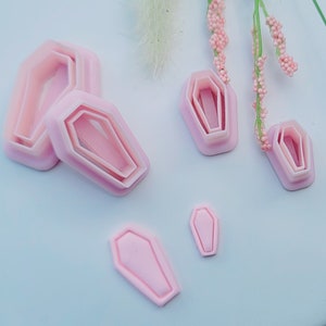 May include: Set of five pink plastic coffin-shaped cookie cutters of varying sizes.