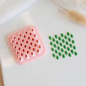Puede incluir: Dos moldes de silicona para hacer fondant o pasta de goma decorativos. Un molde es rosa y tiene forma de diamante con un patrón de pequeñas formas de lágrima. El otro molde es verde y tiene forma de rectángulo con un patrón de pequeñas formas de lágrima.