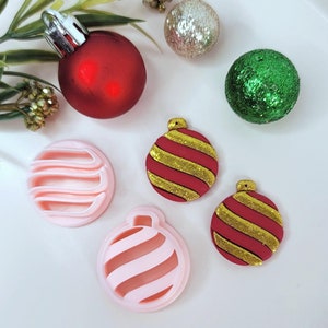 May include: A collection of Christmas ornaments in various styles and colors. Includes a red ball ornament, two pink ornament-shaped cookie cutters, two red and gold striped ornaments, and two glittery ball ornaments in silver and green.