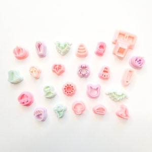 Op de afbeelding: Een verzameling van 20 pastelkleurige plastic koekjesvormen in verschillende vormen, waaronder pompoenen, geesten, vleermuizen, bladeren en bloemen. De vormen zijn gerangschikt op een wit oppervlak.