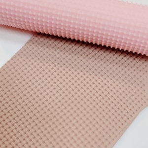 May include: A close-up of a pink silicone rolling pin with a textured surface. The rolling pin is on top of a brown silicone mat with a textured surface.