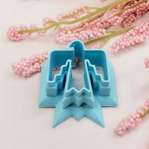 Peut inclure: Un emporte-pièce en plastique bleu clair en forme d'oiseau stylisé avec un design en couches. L'emporte-pièce est sur une surface blanche.