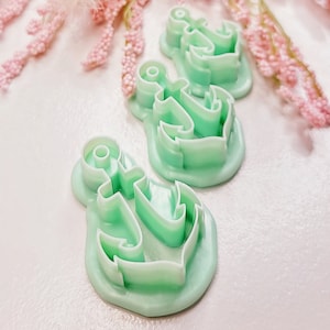 May include: Three green plastic anchor-shaped cookie cutters. The cutters are stacked on top of each other.