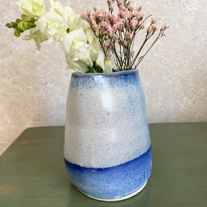 May include: A white ceramic vase with a blue glaze, featuring a textured, speckled finish. The vase is filled with white and pink flowers.