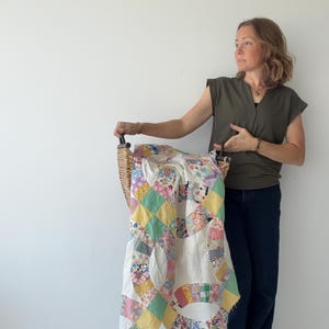 May include: A double wedding ring pattern quilt featuring a variety of colourful floral and checkered fabric patches in shades of yellow, pink, blue, and green, set against a white background, draped over a woven wicker basket.