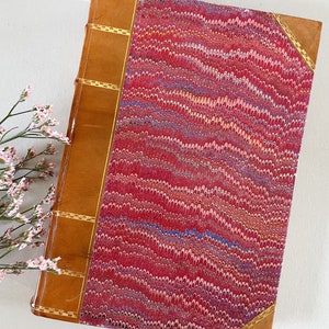May include: A vintage book with a marbled red, pink, and blue cover. The book has a brown leather spine with gold accents.