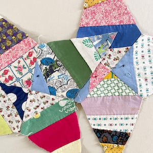 May include: Close-up of a handmade quilt fragment. The quilt features a variety of colorful fabric scraps, including floral, polka dot, and patterned designs. The pieces are sewn together in a geometric pattern, showcasing a mix of pink, blue, green, and yellow hues.