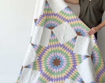 May include: A large quilt featuring a central star pattern composed of small diamond-shaped fabric pieces in pastel shades of yellow, green, blue, and lavender, accented with brown, set against a white background with quilted texture.