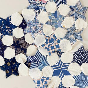 May include: A close-up of a handmade quilt fragment. The quilt features a variety of blue patterned fabrics, including floral, polka dot, and striped designs, with white hexagon shapes. The quilt is a patchwork of different fabrics.