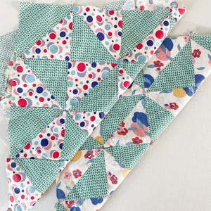 May include: Close-up of two sections of a patchwork quilt in progress. The quilt features a repeating pattern of triangles in various fabrics. Some triangles are teal with a dotted pattern, while others have red, blue, and white circles or floral designs.