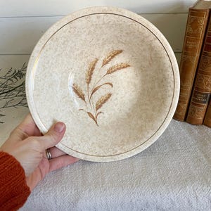 May include: A white ceramic bowl with a brown wheat design. The bowl has a gold rim and a speckled glaze.