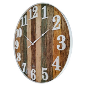 May include: A large, round, white-framed clock with a woodgrain face. The clock face is made of multiple strips of wood in various shades of brown, green, and beige. The numbers are white and are in a simple, blocky font.