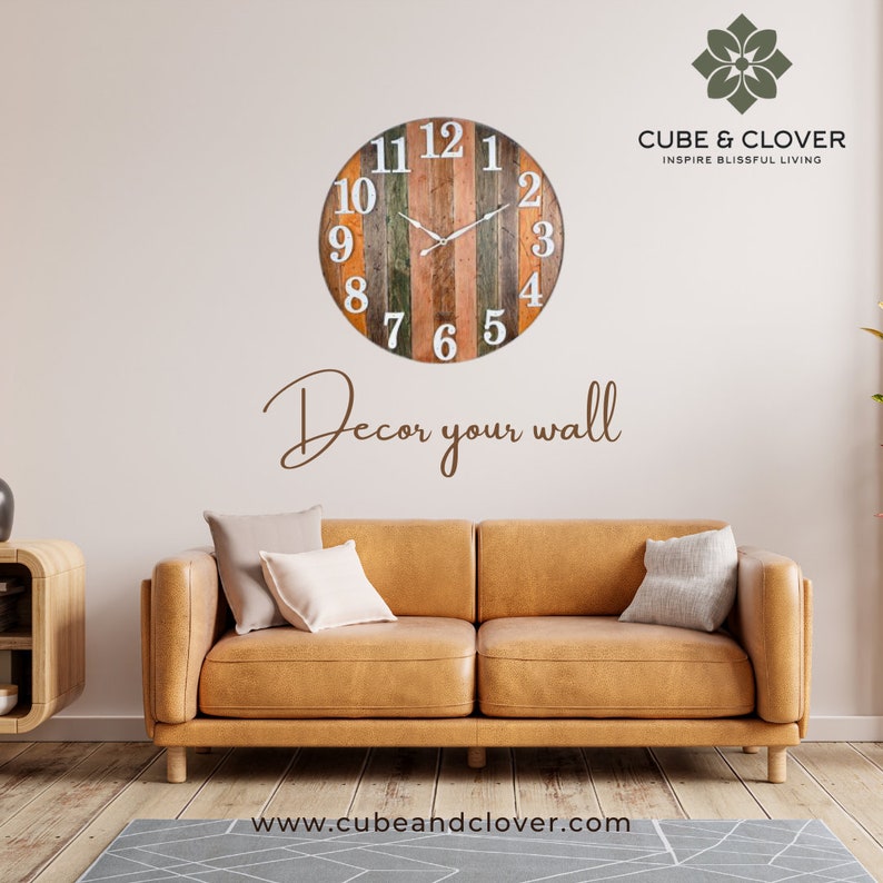 May include: A wooden clock with a rustic design, featuring a multi-colored striped face with white numbers. The clock is hanging on a white wall above a brown leather couch. The text "Decor your wall" is written below the clock. The text "CUBE & CLOVER INSPIRE BLISSFUL LIVING" is written in the top right corner of the image. The text "www.cubeandclover.com" is written at the bottom of the image.