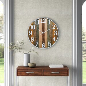 May include: A round wall clock with a white face and black hands. The clock face is made of wood planks in various shades of brown, green, and beige. The numbers are white and outlined in black.