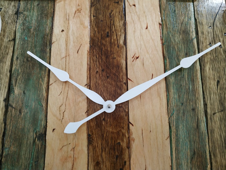 May include: White clock hands on a wooden background. The wood is a mix of light and dark brown with green accents.