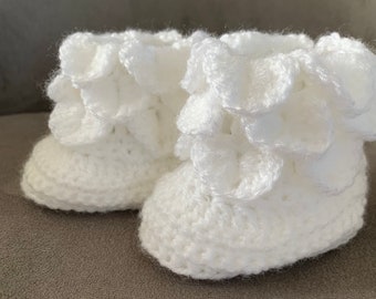 Puede incluir: Un par de botitas de bebé blancas de ganchillo con bordes con volantes.