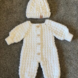 Puede incluir: Un pelele de manga larga de ganchillo blanco con patr&oacute;n texturizado, cuatro botones de color marr&oacute;n claro con forma de oso en la parte delantera y pu&ntilde;os acanalados. Incluye un gorro de ganchillo blanco a juego con pomp&oacute;n y etiqueta MADE WITH.