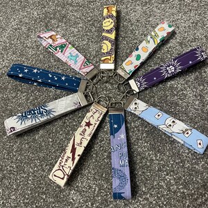 May include: A selection of key fobs with diverse patterns and designs. The key fobs display various colours and themes, including stars, owls, and text. Each fob has a metal clasp for attaching keys.