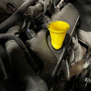 May include: A yellow plastic funnel with the text "GM L/B 6.6L" printed on the side, inserted into the opening of a black engine block.